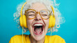 © Poj - An elderly woman with yellow headphones enjoys listening to the music, laughing with happiness against blue background.