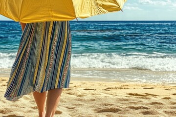 Wall Mural - Woman with striped dress holding yellow umbrella on sandy beach by ocean
