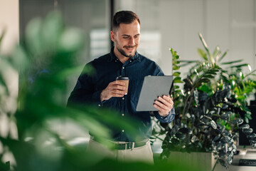 Portrait of smiling manager with tablet drinking coffee at green office