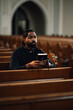 © Zamrznuti tonovi - Priest holding rosary beads and bible sitting in church pew