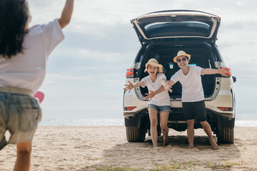 Asian family of three is playing on the beach on back car, with a young girl running towards car. Father and mother open their arms to welcome their daughter running towards them, summer trip concept