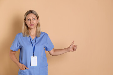 Canvas Print - Nurse in medical uniform with badge showing thumbs up on beige background