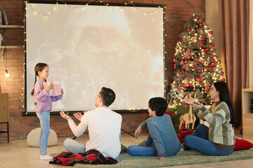 Wall Mural - Happy family with popcorn watching Christmas movie on projector screen at home, back view