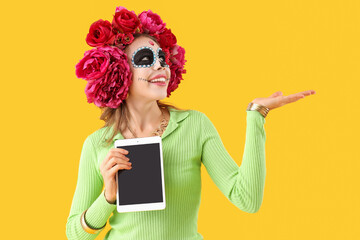 Wall Mural - Young woman with tablet computer showing something on yellow background. Mexico's Day of the Dead (El Dia de Muertos) celebration