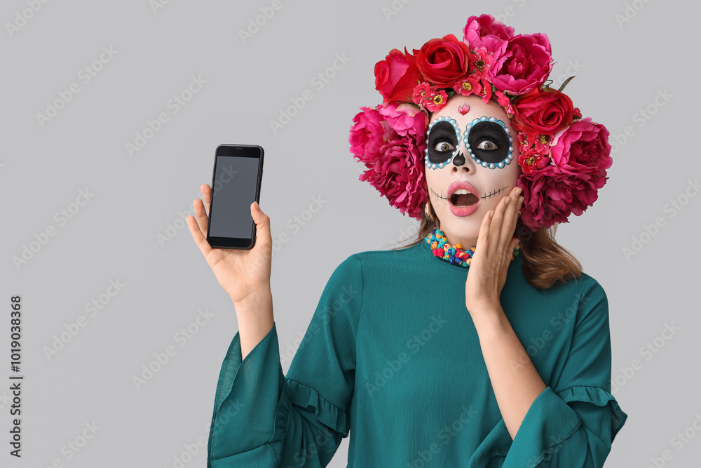 Shocked young woman with mobile phone on light background. Mexico's Day of the Dead (El Dia de Muertos) celebration