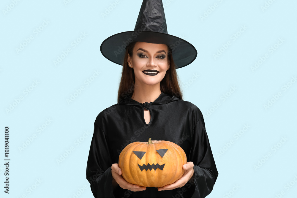 Young woman dressed for Halloween as witch with pumpkin on blue background