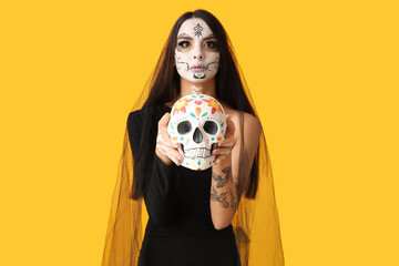 Wall Mural - Young woman dressed as dead bride for Halloween party with painted human skull on yellow background