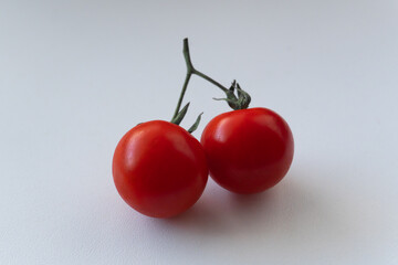 A branch with two cherry tomatoes resembling cherries on a white background. Rich cherry tomatoes rest on a light backdrop. Fresh vegetables of natural origin.