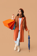 Wall Mural - Young woman with shopping bags and umbrella on brown background