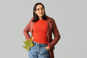 Poster - Beautiful young woman with autumn leaves on grey background