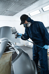 Painting cars in vehicle maintenance service using paint sprayer. Car painter is using HVLP or LVLP spray gun to apply paint on metal.