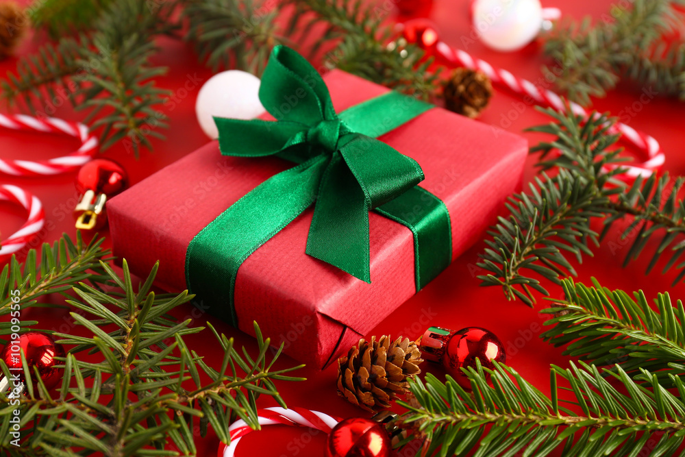 Christmas gift box with balls, fir tree branches and candy cane toys on red background