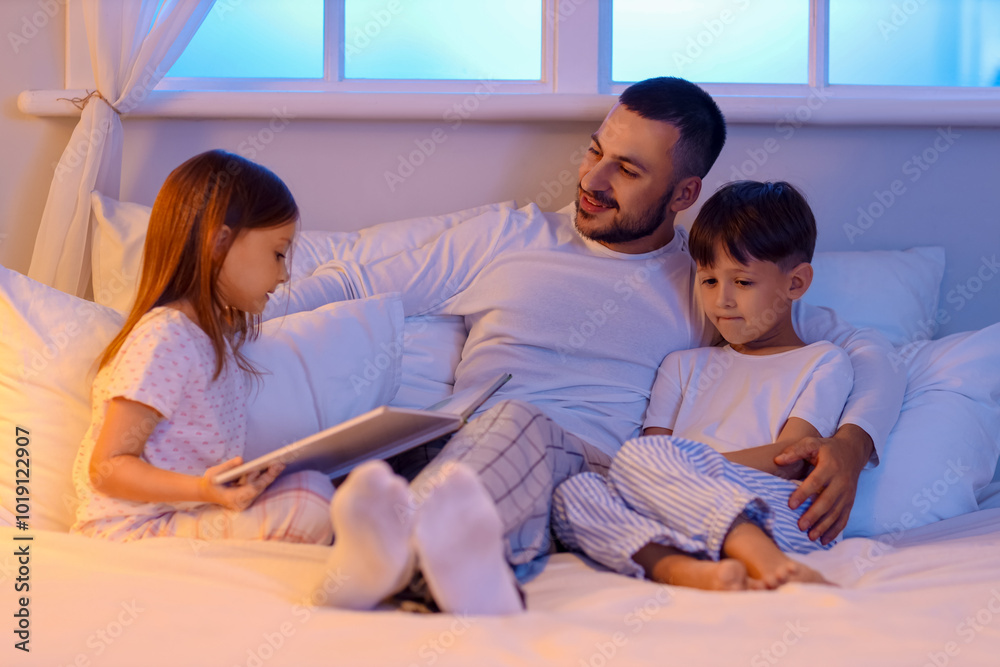 Young man reading bedtime story to his children in bed