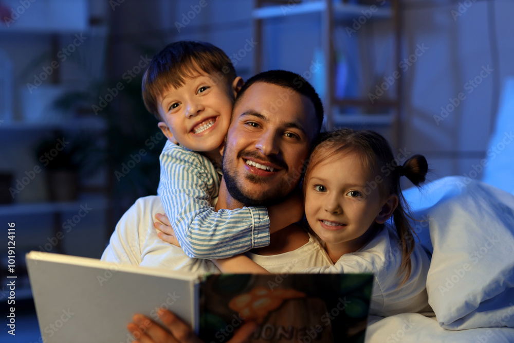 Young father reading book for his children in bed