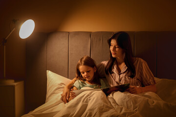 Poster - Happy mother and her little daughter reading fairy-tale in bed at night