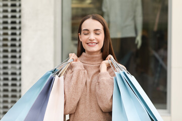 Beautiful young happy woman with shopping bags near clothing store on city street. Black Friday sale