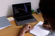 © Oleksii Syrotkin/Stocksy - Partial man watching market graph on laptop and writing in notebook