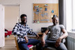 © Oleksii Syrotkin/Stocksy - Smiling black men looking at camera during sitting in chairs at home