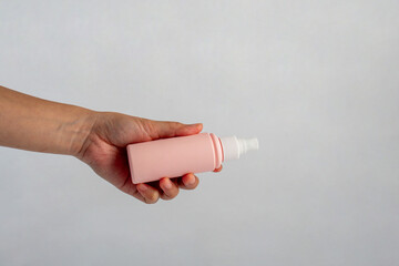 Canvas Print - Cosmetic pink bottle and hand, bottle, lotion or serum with stylish props on white background. 