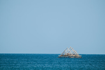 Traditional Floating Bagan Amidst Vast Blue Ocean. Serene Summer Waves Under Bright Blue Skies. Traditional fish aggregating device, bamboo fish trap.