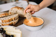 © Adrian Cotiga/Stocksy - Hand dipping bread slice into creamy orange dip bowl.
