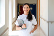 © Santi Nuñez/Stocksy - Smiling nurse holding a tablet in a hospital corridor