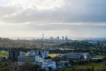 A sweeping aerial view of Auckland’s urban landscape, showcasing the city's iconic Sky Tower amidst a backdrop of sprawling residential areas and natural harbors under a bright sky