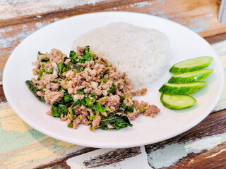 Thai street food concept. Minced pork with basil and cucumber sliced served with rice on a white plate.