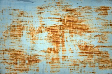 A rusty metal surface with a blue background. The surface is covered in scratches and has a worn appearance