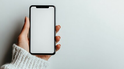 A hand in a sweater holds a smartphone with a blank screen on a white background.