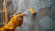 © kayudamar - A Close-Up Of A Hand In A Yellow Glove Painting A Concrete Wall With A Brush