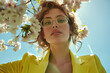 © Femmes.Digital - Portrait of a woman in a yellow outfit with glasses, surrounded by spring blossoms. A stylish, nature-inspired fashion look.