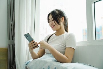 Wall Mural - Image of young Asian girl using phone and relaxing in bed