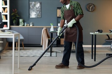 Side view cropped shot of male cleaner vacuuming floors in home or office interior, copy space