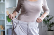 © Liubomir - Woman showing weight loss achievement by holding oversized pants. Concept of fitness success, healthy lifestyle, diet, and personal transformation indoors.