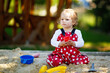 © Irina Schmidt - Cute toddler girl playing in sand on outdoor playground. Beautiful baby in red gum trousers having fun on sunny warm summer day. Child with colorful sand toys. Healthy active baby outdoors plays games