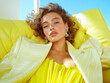 © Femmes.Digital - Close-up of a model in a yellow outfit reclining on a vibrant yellow couch. A glamorous, sunny fashion moment with a modern edge.