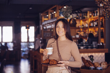 Portrait of an adult young beautiful brunette girl in a cafe with a cup of coffee and a croissant