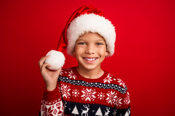 Poster - Photo portrait of charming small boy touch hold pompom celebrate christmas dressed knitted sweater isolated on red color background