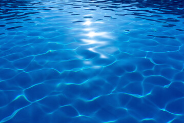 Blue ripped water in swimming pool with sun reflection