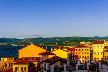 beautiful cityscape with town during sunset with blue see gulf and harbor with boats, calm water and green scenic hills with amazing cloudy sky on background