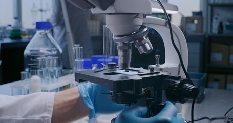 Medical science laboratory: Close up of professional microbiologist or scientist in gloves putting glass slide with test sample under microscope for analysis, developing drugs. High-tech lab device.