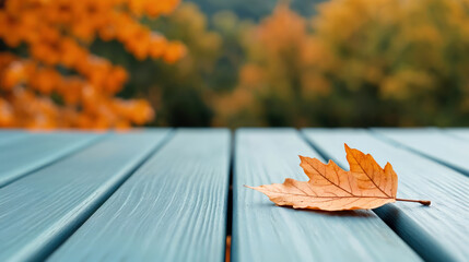 Poster - Lonely autumn leaf resting on empty blue table outdoors
