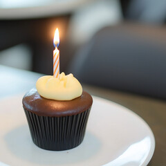 A simple elegant close-up of a cupcake with a single lit candle, symbolizing celebration or a birthday. The minimal background and soft focus enhance the sense of warmth, simplicity, special occasion