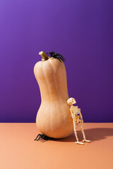 Halloween pumpkin with black spiders and plastic skeleton on purple and orange background. Creative Halloween concept