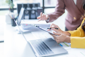 Two businesswomen are working together in the office, analyzing financial documents and pointing at a chart on a clipboard