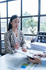 Two businesswomen collaborating in the office, analyzing financial reports and crunching numbers with a calculator during a productive meeting