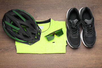 Poster - Bicycle helmet, sneakers, goggles and shirt on wooden background, flat lay