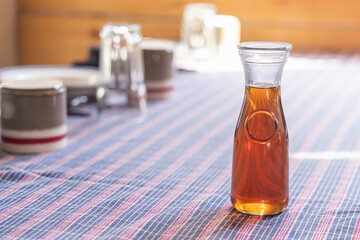 Maple syrup in glass bottle sitting on a table with a blue and red tablecloth, set for breakfast. Selective focus