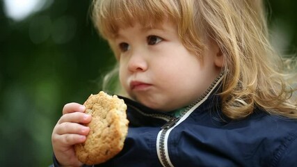 Wall Mural - A cute baby eats bread. Hungry little kid eating kids food. Baby bread. Meal time. Little baby eating healthy food. A Little baby eating her dinner outdoor. Close-up portrait of kid with bread.